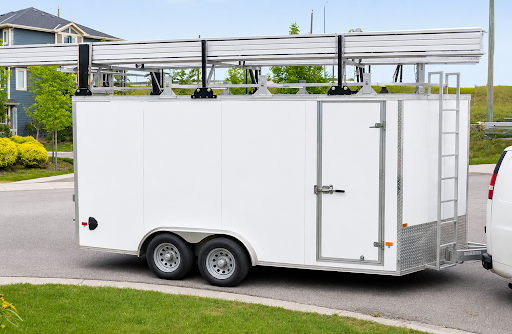 White enclosed cargo trailer with tandem axles and rooftop ladder rack parked in a residential neighborhood, showcasing durable enclosed trailers in Carolina for secure equipment and cargo transport.