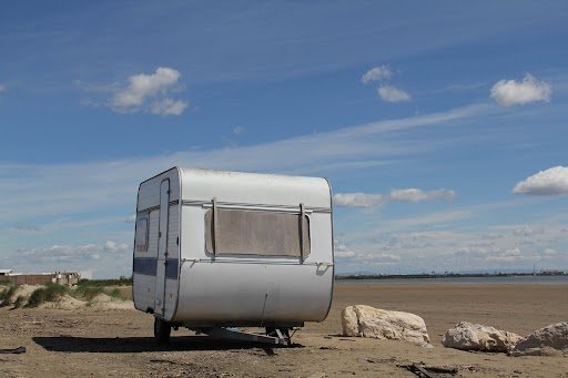 White enclosed travel trailer parked on a sandy coastal landscape under a bright blue sky, showcasing durable enclosed trailers in Carolina designed for secure transport, storage, and outdoor adventures.