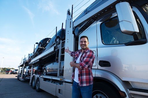 Smiling driver standing beside a professional car carrier truck loaded with vehicles, showcasing dependable car hauler trailers in Carolina for safe and efficient auto transport.